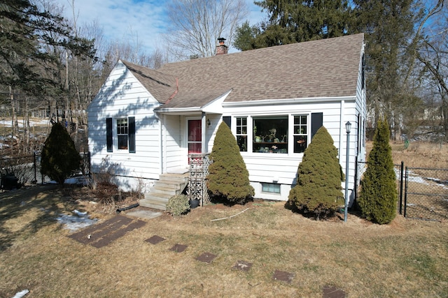 view of front of property featuring a front yard, roof with shingles, fence, and a chimney