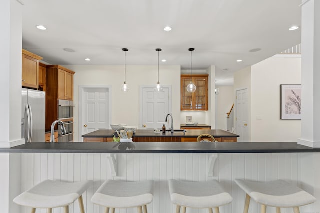 kitchen with brown cabinets, dark countertops, a sink, stainless steel fridge with ice dispenser, and a kitchen island with sink