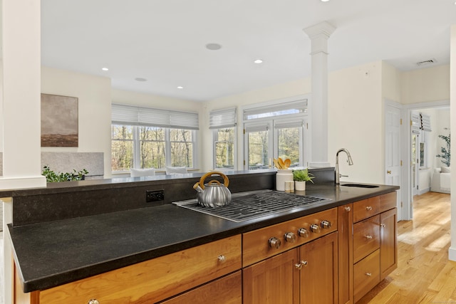 kitchen featuring dark countertops, a sink, light wood-style flooring, stainless steel gas stovetop, and visible vents
