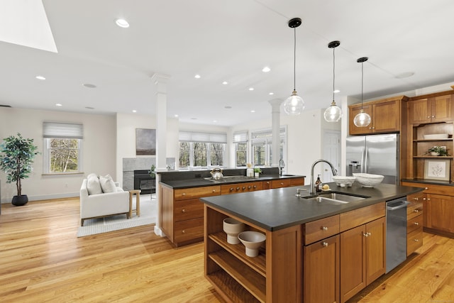 kitchen featuring open shelves, a kitchen island with sink, dark countertops, a sink, and appliances with stainless steel finishes