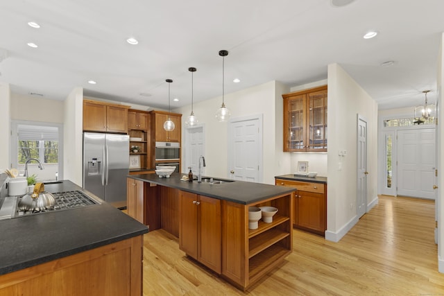 kitchen with open shelves, appliances with stainless steel finishes, dark countertops, a sink, and light wood-type flooring