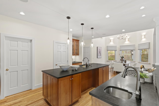 kitchen with brown cabinets, dark countertops, a sink, an island with sink, and glass insert cabinets