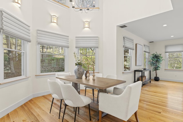 dining space featuring a towering ceiling, visible vents, wood finished floors, baseboards, and an inviting chandelier