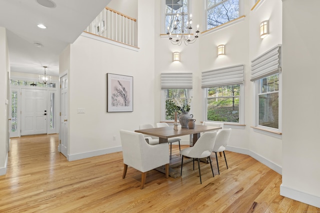 dining space featuring baseboards, light wood-style flooring, a high ceiling, and a notable chandelier