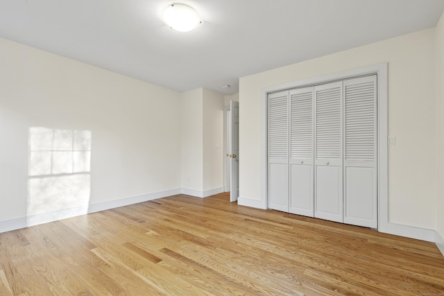 unfurnished bedroom featuring light wood-style floors, baseboards, and a closet