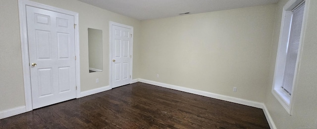 unfurnished bedroom with visible vents, baseboards, and dark wood-type flooring