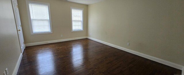 empty room with dark wood-style flooring and baseboards