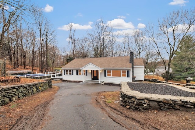 view of front facade featuring aphalt driveway, fence, a chimney, and a shingled roof