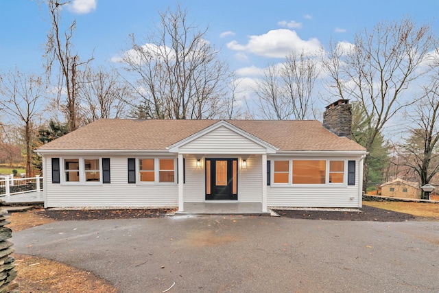 view of front of home with aphalt driveway, covered porch, roof with shingles, and a chimney