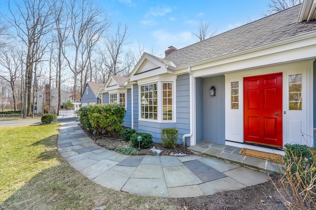 property entrance with roof with shingles, a yard, and a chimney