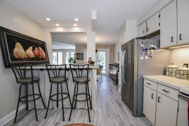 kitchen with freestanding refrigerator, white cabinets, and a kitchen breakfast bar