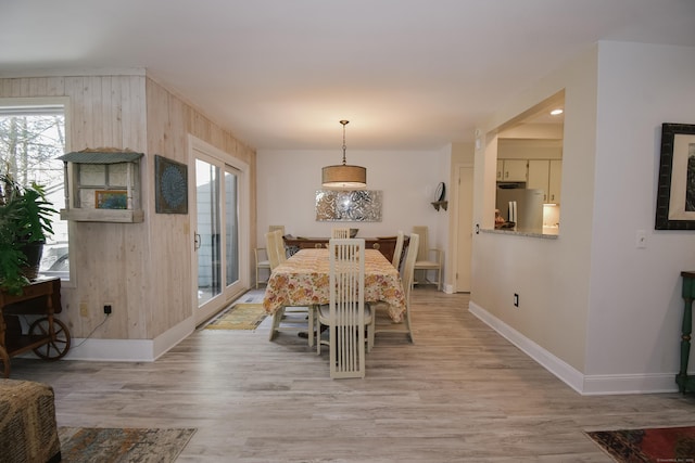 dining room with light wood finished floors, wood walls, and baseboards