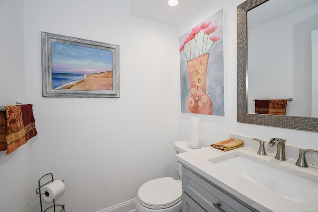 half bathroom with baseboards, vanity, and toilet