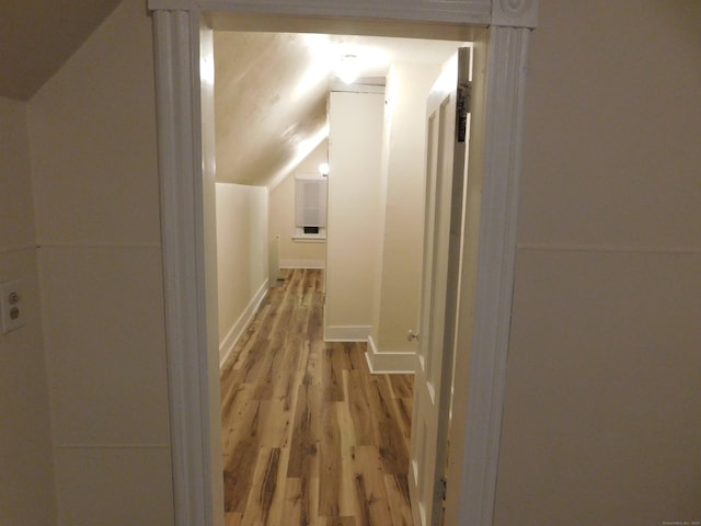 hall with light wood-style floors and vaulted ceiling