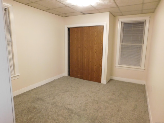 unfurnished bedroom featuring a paneled ceiling, a closet, carpet floors, and baseboards