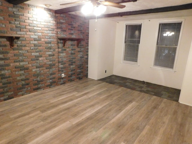 spare room with beam ceiling, wood finished floors, and brick wall