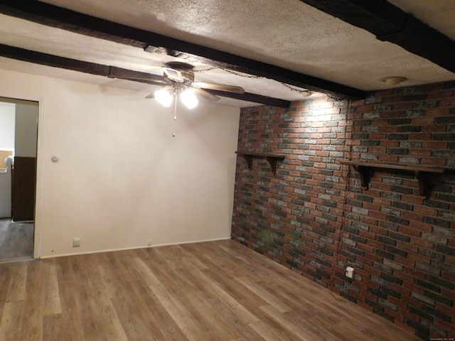 empty room featuring beamed ceiling, a ceiling fan, a textured ceiling, wood finished floors, and brick wall