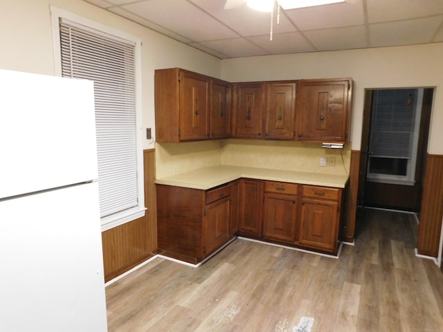 kitchen featuring brown cabinetry, light wood-style flooring, freestanding refrigerator, light countertops, and wainscoting