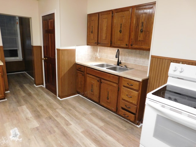 kitchen with brown cabinetry, a wainscoted wall, white electric range, and a sink