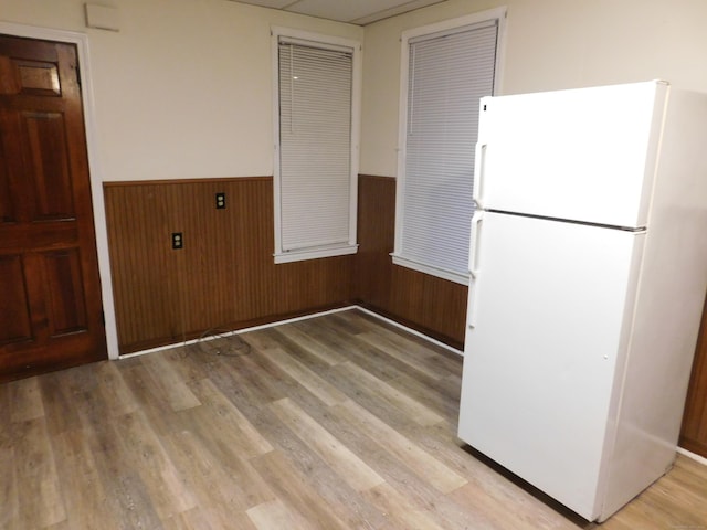 kitchen with a wainscoted wall, light wood finished floors, wooden walls, and freestanding refrigerator