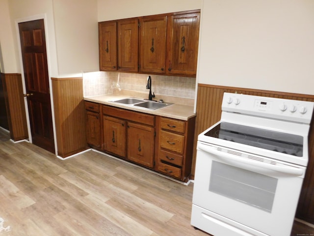 kitchen with a sink, light countertops, electric stove, wainscoting, and brown cabinets