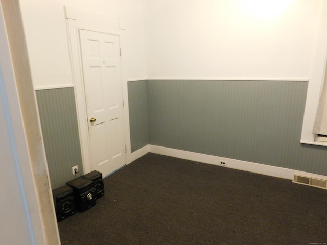 empty room featuring a wainscoted wall, dark carpet, and visible vents