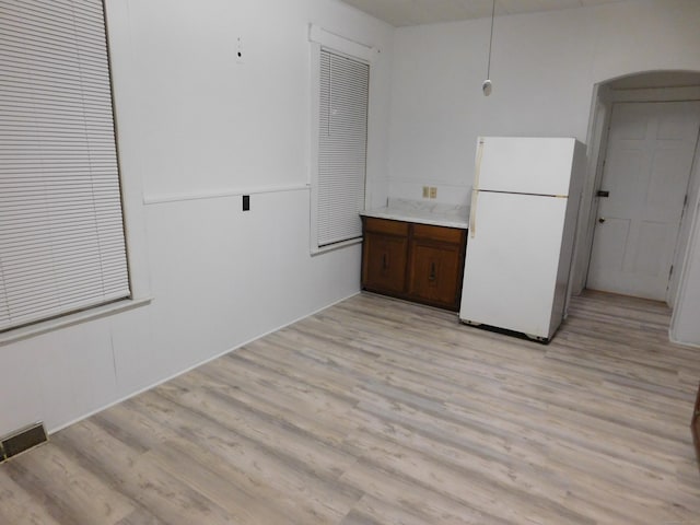 kitchen with visible vents, light wood-style flooring, freestanding refrigerator, arched walkways, and light countertops