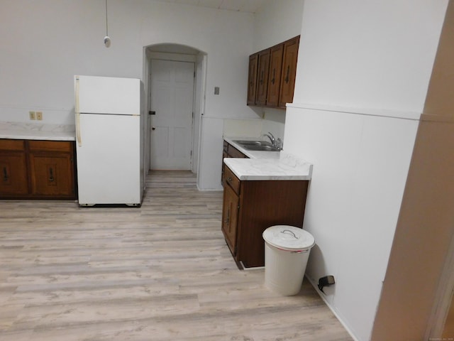 kitchen featuring light wood finished floors, light countertops, freestanding refrigerator, and a sink