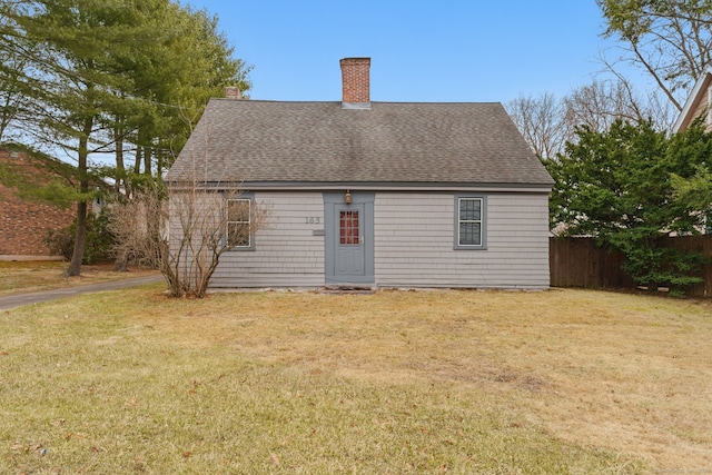 rear view of house featuring a yard, roof with shingles, a chimney, and fence