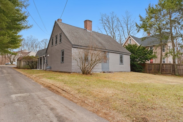 view of home's exterior featuring roof with shingles, fence, a chimney, and a lawn