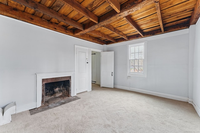 unfurnished living room featuring carpet floors, beam ceiling, a fireplace with flush hearth, wood ceiling, and baseboards