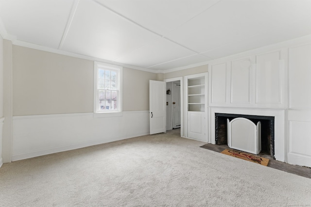 unfurnished living room featuring built in features, wainscoting, a fireplace with flush hearth, carpet, and crown molding