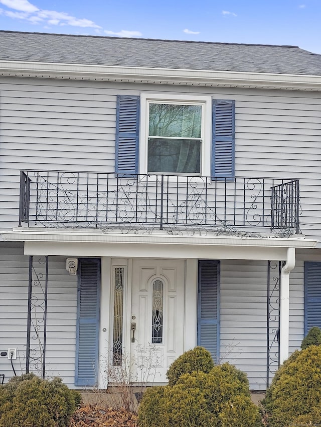 view of front facade with a shingled roof and a balcony