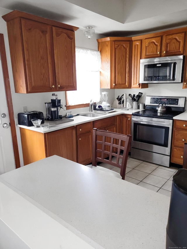 kitchen with brown cabinetry, stainless steel appliances, a sink, and light countertops