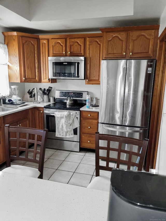 kitchen with appliances with stainless steel finishes, light countertops, brown cabinets, and light tile patterned floors