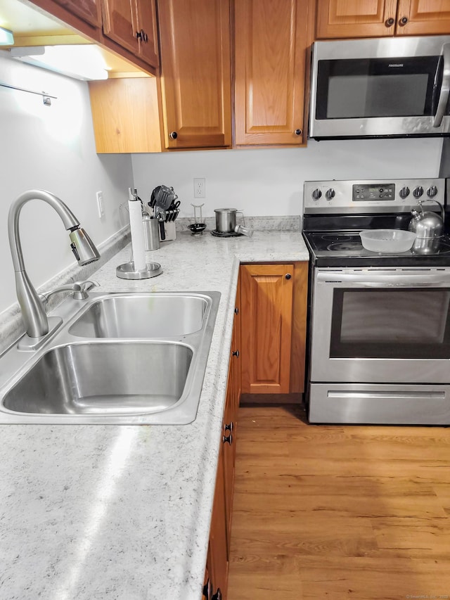 kitchen with appliances with stainless steel finishes, brown cabinets, a sink, and light wood-style flooring