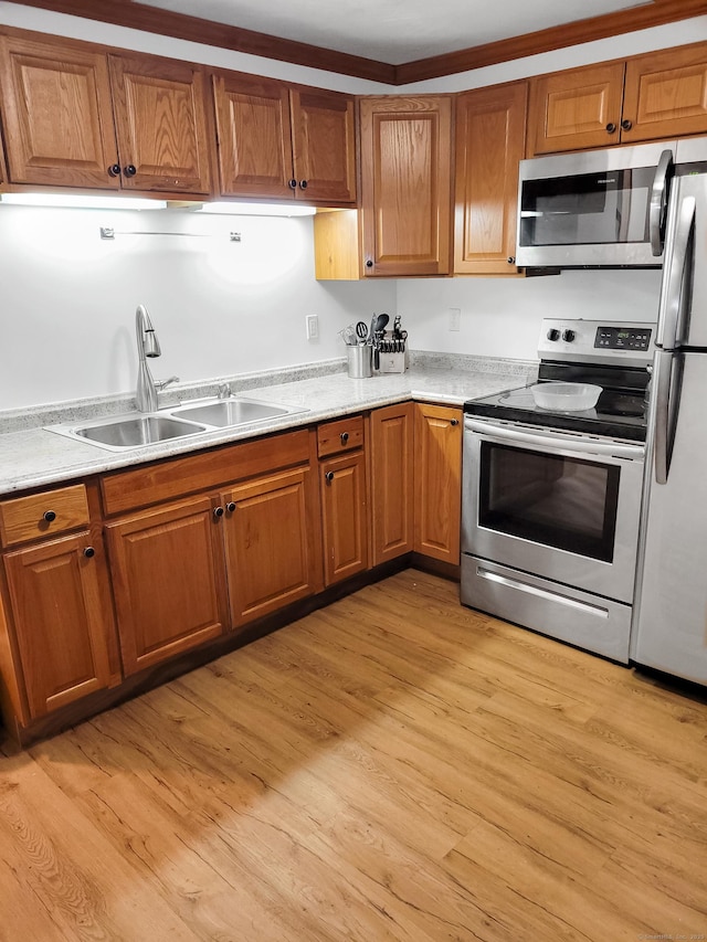 kitchen with appliances with stainless steel finishes, brown cabinetry, a sink, and light wood finished floors