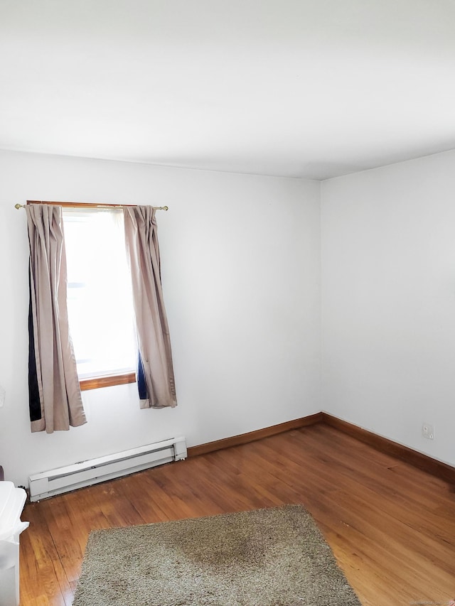 unfurnished room featuring a baseboard heating unit, wood finished floors, and baseboards