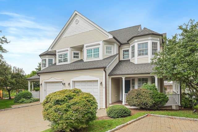 view of front of property featuring a porch, a shingled roof, decorative driveway, and an attached garage