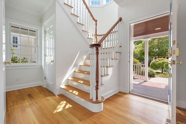 entrance foyer with ornamental molding, baseboards, light wood finished floors, and stairs