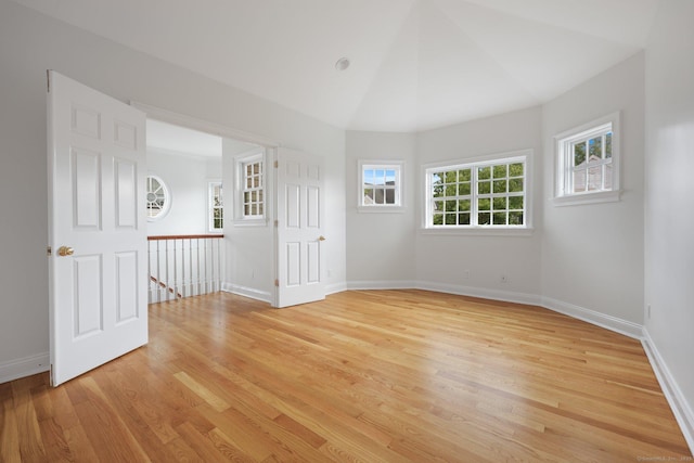 spare room with light wood-type flooring, lofted ceiling, and baseboards