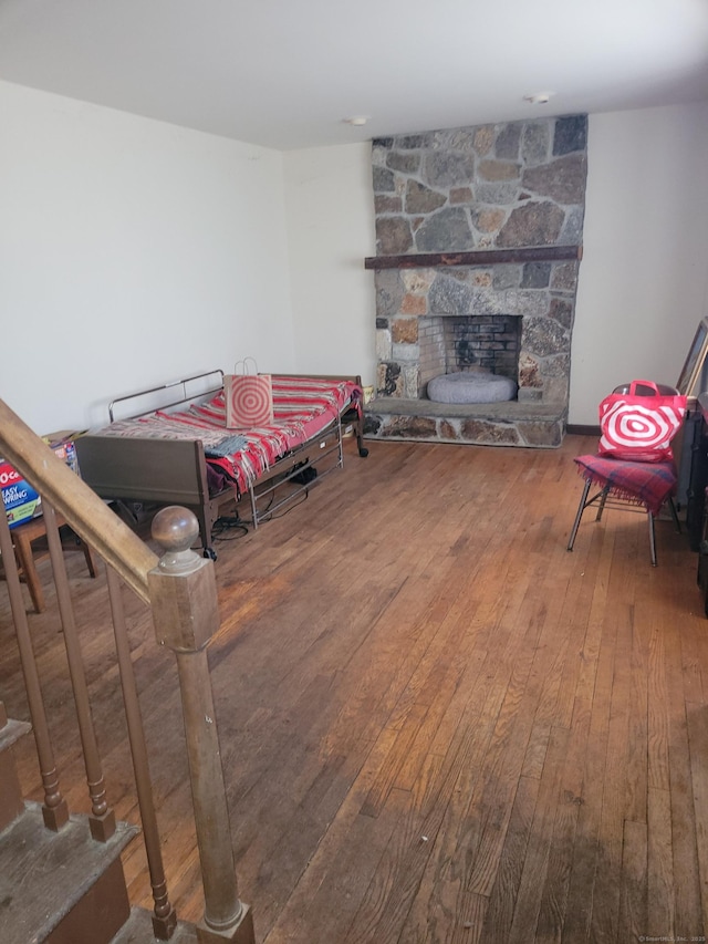 living area with wood-type flooring, stairs, and a stone fireplace