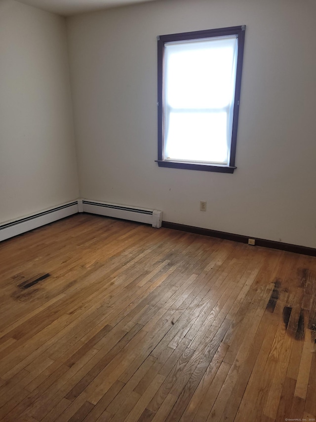 spare room featuring a baseboard heating unit, wood-type flooring, and baseboards