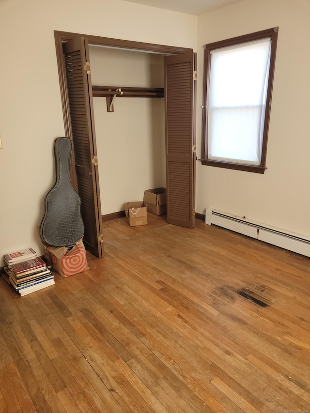 unfurnished bedroom with a closet, baseboards, light wood-style flooring, and baseboard heating