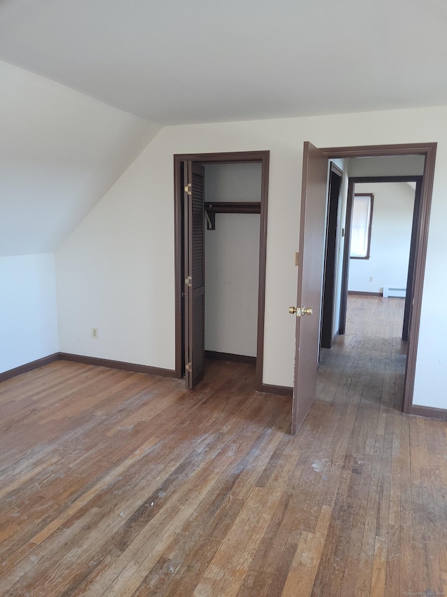 unfurnished bedroom featuring a baseboard radiator, baseboards, vaulted ceiling, a closet, and hardwood / wood-style floors