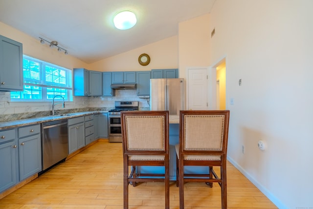 kitchen featuring light wood-type flooring, a sink, under cabinet range hood, appliances with stainless steel finishes, and decorative backsplash