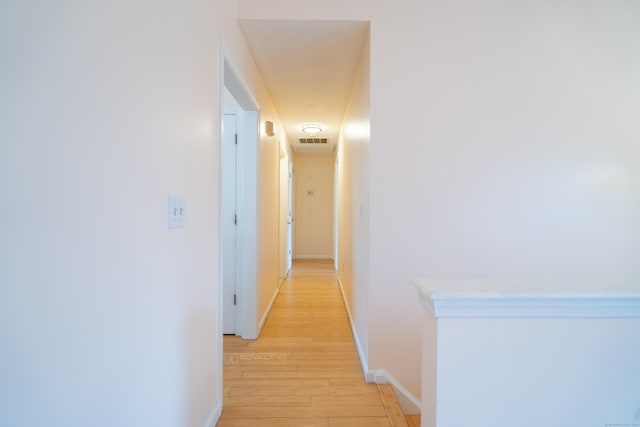 hall featuring light wood-type flooring, baseboards, and visible vents