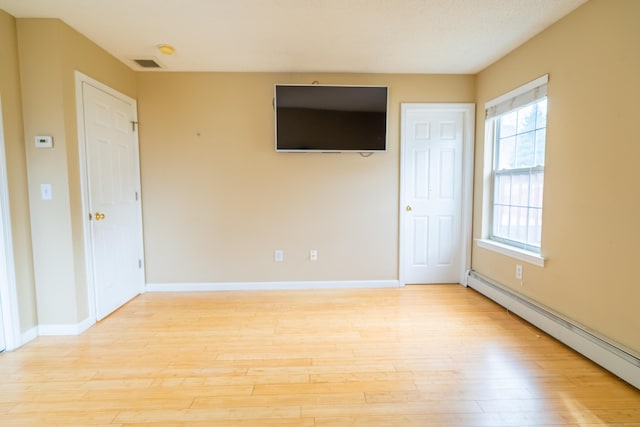 spare room featuring a baseboard heating unit, baseboards, visible vents, and light wood-style flooring