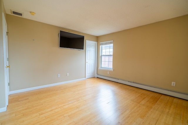 empty room featuring a baseboard heating unit, baseboards, visible vents, and wood finished floors