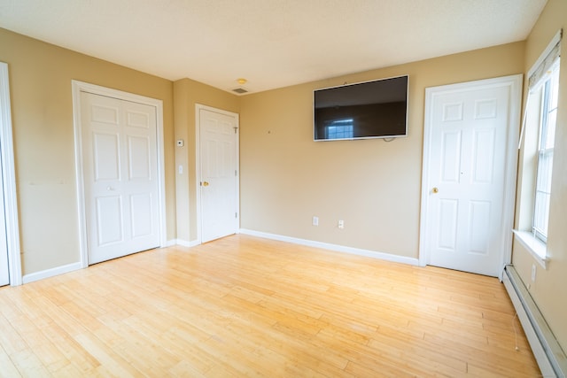 unfurnished bedroom featuring a baseboard radiator, baseboards, and light wood-style floors